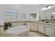 Bathroom with a tub, granite counters, white cabinets, and a large window with plantation shutters at 13408 Swiftwater Way, Bradenton, FL 34211