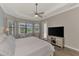 This bedroom features a ceiling fan, entertainment center, and expansive windows overlooking the lake at 20686 Valprato Ct, Venice, FL 34293