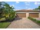 Two-car garage with paver driveway, lush landscaping, and Spanish-style tile roof at 114 Babbling Brook Run, Bradenton, FL 34212