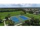 Aerial view of two well-maintained tennis courts surrounded by lush green landscaping in a quiet neighborhood at 10817 56Th St E, Parrish, FL 34219