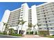 Scenic view of a white high-rise condo building with manicured landscaping and palm trees against a blue sky at 9397 Midnight Pass Rd # 603, Sarasota, FL 34242