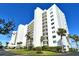 Striking view of a high-rise condo building with manicured grounds and palm trees against a clear blue sky at 9397 Midnight Pass Rd # 603, Sarasota, FL 34242