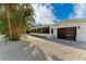 Front view of a single-story home with a modern garage door and tropical landscaping at 115 Los Cedros Dr, Anna Maria, FL 34216