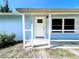 Front porch with white door featuring glass panes and white pillars, contrasting against the light blue wall at 712 N Elm St, Englewood, FL 34223