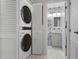 Hallway laundry closet with stacked washer and dryer next to a bathroom with leaf wallpaper at 6609 Stone River Rd # 206, Bradenton, FL 34203