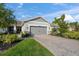 Single-story home with gray garage door and paver driveway; landscaping includes lush green grass and bushes at 8669 Rain Song Rd, Sarasota, FL 34238