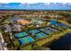 Aerial view of community amenities, including tennis and pickleball courts, clubhouse, and pool, surrounded by lush landscaping and a lake at 6063 Benevento Dr, Sarasota, FL 34238