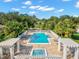 Aerial view of the community pool and jacuzzi, surrounded by lush tropical landscaping and patio furniture at 7327 Kensington Ct, University Park, FL 34201