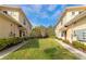 Well-manicured backyard area featuring green grass between tan townhomes under a blue sky at 8362 Enclave Way # 103, Sarasota, FL 34243