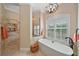 Bright bathroom with modern tile shower, chandelier, and a free standing tub with shuttered window at 2023 Micanopy Trl, Nokomis, FL 34275