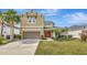 Two-story tan home featuring a landscaped yard, two-car garage, and a welcoming red double-door entrance at 5718 Westhaven Cv, Bradenton, FL 34203