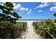 Scenic beach access through greenery to a serene beach with blue skies and ocean views at 104 Inlets Blvd # 104, Nokomis, FL 34275