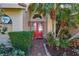 A red double-door entry is framed by lush tropical landscaping and a brick pathway leading to the home at 104 Inlets Blvd # 104, Nokomis, FL 34275