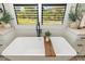 Bright bathroom featuring a luxurious soaking tub, white cabinets, and a window with shutters at 20078 Elegante Ct, Venice, FL 34293