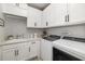 Convenient laundry room with white cabinets, mosaic backsplash, sink, and modern washer and dryer at 20078 Elegante Ct, Venice, FL 34293