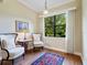 Bright sitting room with hardwood floors, two chairs, side table, and a window with a view of lush greenery at 20909 Loggia Ct, Venice, FL 34293