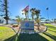 Inviting community entrance with well-maintained landscaping, palm trees and a prominent sign with the American flag flying above at 607 Baronet Ln, Holmes Beach, FL 34217