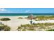 Tranquil beach scene with white sand, turquoise water, and a tiki hut with chairs and table at 1211 Gulf Of Mexico Dr # 701, Longboat Key, FL 34228