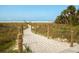 Picturesque beach access path with rope fencing leading to a white sand beach and clear blue sky at 4822 Ocean Blvd # 2D, Sarasota, FL 34242