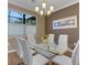 Elegant dining room with a glass table, seating for six, a modern chandelier, and natural light from the window at 5946 Caspian Tern Dr, Sarasota, FL 34238