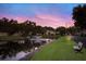 Community pond view featuring a water fountain, bench, green grass and colorful skies above nearby residential street at 2720 60Th Avenue W Dr # D, Bradenton, FL 34207