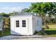 A well-lit, white storage shed on a brick pad, accented by lush greenery and a mature shade tree at 222 Pine Glen Ct, Englewood, FL 34223