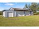 Exterior shot of the detached garage, featuring three bays, a grey exterior, and a well-kept lawn at 25605 69Th E Ave, Myakka City, FL 34251