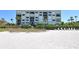 Condo building on a white sand beach with lounge chairs, palm trees, and manicured hedges at 2675 Gulf Of Mexico Dr # 301, Longboat Key, FL 34228