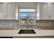Close up of kitchen sink looking out the window with white cabinets and mosaic backsplash at 5115 Island Date Way, Sarasota, FL 34232