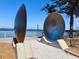 Public art sculpture featuring a large metal disc with an industrial design set along a waterfront at 1520 2Nd E Ave, Bradenton, FL 34208