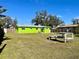 Backyard featuring lush green grass, mature trees, and the vibrant green exterior of the single-story home at 30431 Holly Rd, Punta Gorda, FL 33982