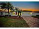 Charming one-story home with a brick driveway and palm trees during sunset at 6049 Grand Cypress Blvd, North Port, FL 34287