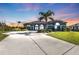 Gray house with palm trees and a large driveway at sunset at 18138 Eau Gallie Cir, Port Charlotte, FL 33948