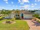 Charming waterfront home featuring a manicured lawn, brick driveway, lush landscaping, and a beautiful blue accent front door at 400 Coronado Dr, Punta Gorda, FL 33950