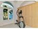 Bright exercise area features an elliptical machine, arched window with palm tree view, and built-in wood cabinets at 18181 Bly Ave, Port Charlotte, FL 33948