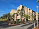 Beige condo building featuring manicured landscaping, palm trees, and clear blue skies at 3006 Caring Way # 409, Port Charlotte, FL 33952