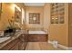 A bathtub with wooden trim and a glass block window, with a granite vanity in the foreground at 1620 Lancashire Dr, Venice, FL 34293