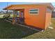 Exterior view of the house with an orange exterior, a small patio, a well-maintained lawn, and some tropical plants at 520 Sharon Cir, Port Charlotte, FL 33952