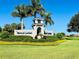 Community entrance sign amidst well-manicured landscaping, palm trees, and blue skies at 25197 Keygrass Ct, Punta Gorda, FL 33955