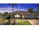 Inviting home exterior featuring a manicured lawn, arched windows, and a well-lit entry at dusk at 27566 Tierra Del Fuego Cir, Punta Gorda, FL 33983