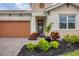 House entrance with orange garage door and lush landscaping at 305 Daylily Blvd, Nokomis, FL 34275