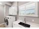 Bright laundry room features white cabinets, modern appliances, a sink and a window with shutters at 9861 Eagle Preserve Dr, Englewood, FL 34224