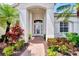 Front entry of the home with a brick walkway, lush landscaping, and a white door at 13760 Long Lake Ln, Port Charlotte, FL 33953