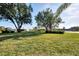 Lush green backyard with trees and manicured lawn offers view to pond and neighboring homes at 1443 Quail Lake Dr, Venice, FL 34293