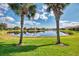 Picturesque backyard with lush green lawn, pond view, and palm trees creating a peaceful setting at 13347 Golf Pointe Dr, Port Charlotte, FL 33953