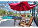 Relaxing poolside view with outdoor seating under a red umbrella, overlooking the lake at 13347 Golf Pointe Dr, Port Charlotte, FL 33953