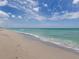 Serene beach view with gentle waves lapping the sandy shore under a bright blue sky with scattered clouds at 5006 Southern Pine Cir, Venice, FL 34293