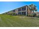 Tan building exterior with screened balconies, lush landscaping, and a grassy lawn at 10055 Crooked Creek Dr # 102, Venice, FL 34293