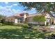 Single-story home with tan walls and a red tile roof, showcasing lush landscaping at 115 Avalini Way, North Venice, FL 34275