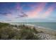 Picturesque beach scene with tranquil ocean waters and tall grassy dunes under a colorful sky at 1200 Tarpon Center Dr # 108, Venice, FL 34285